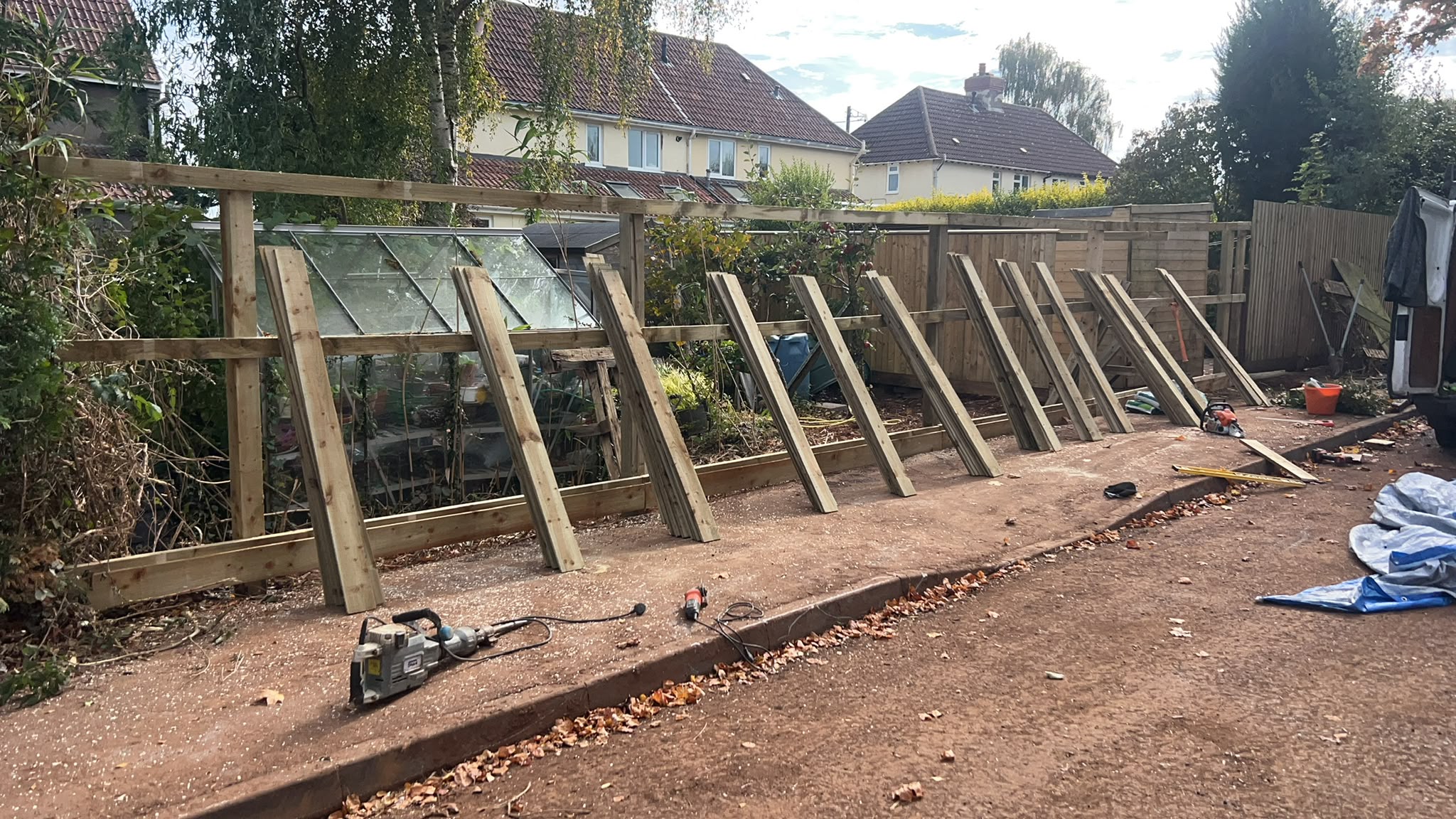 Wooden fence under construction with posts and rails erected and featheredge boards stacked ready, tools on the ground