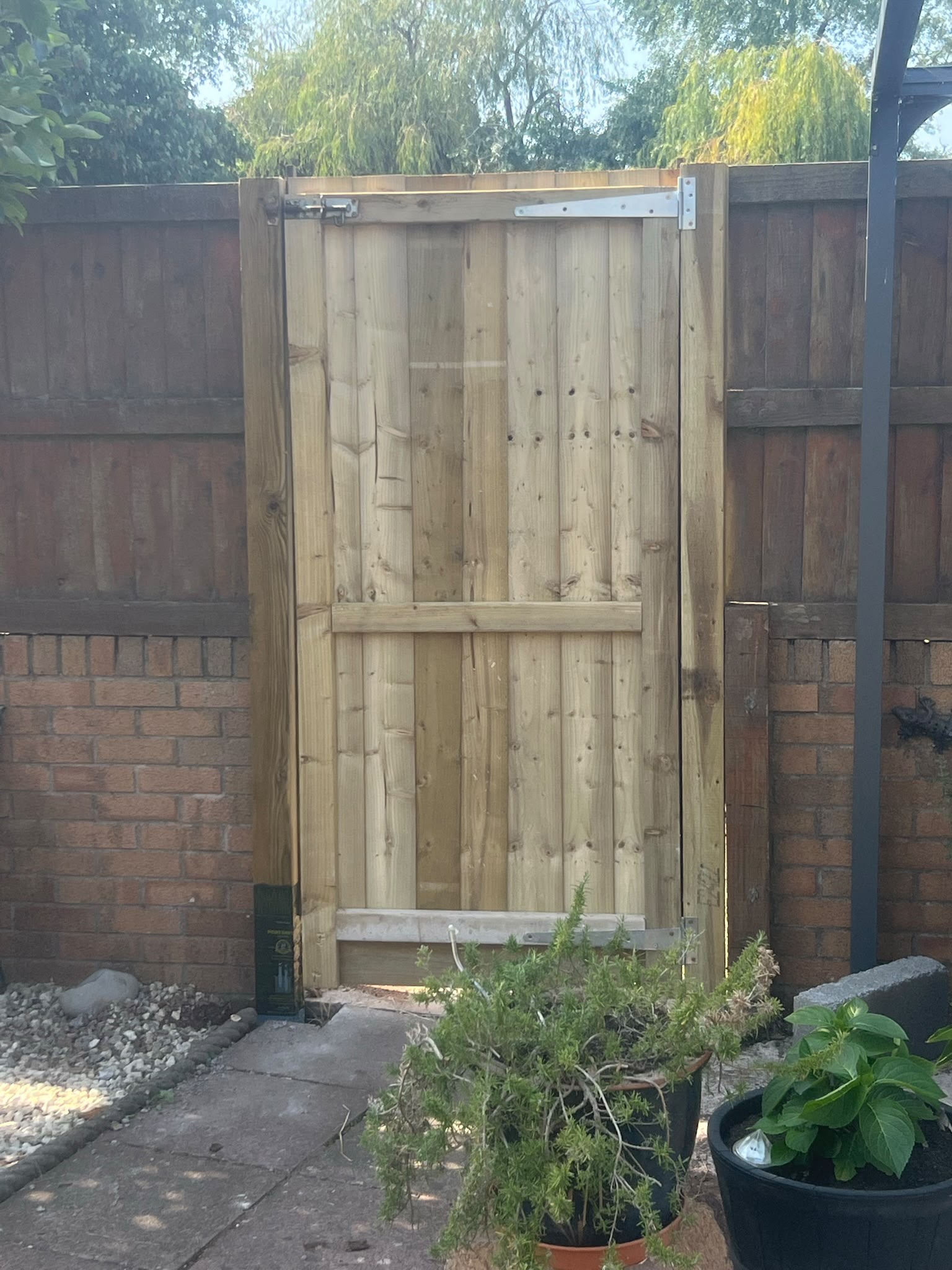 Newly installed light timber closeboard gate with silver hinges and bolt latch set in a brick and wood boundary