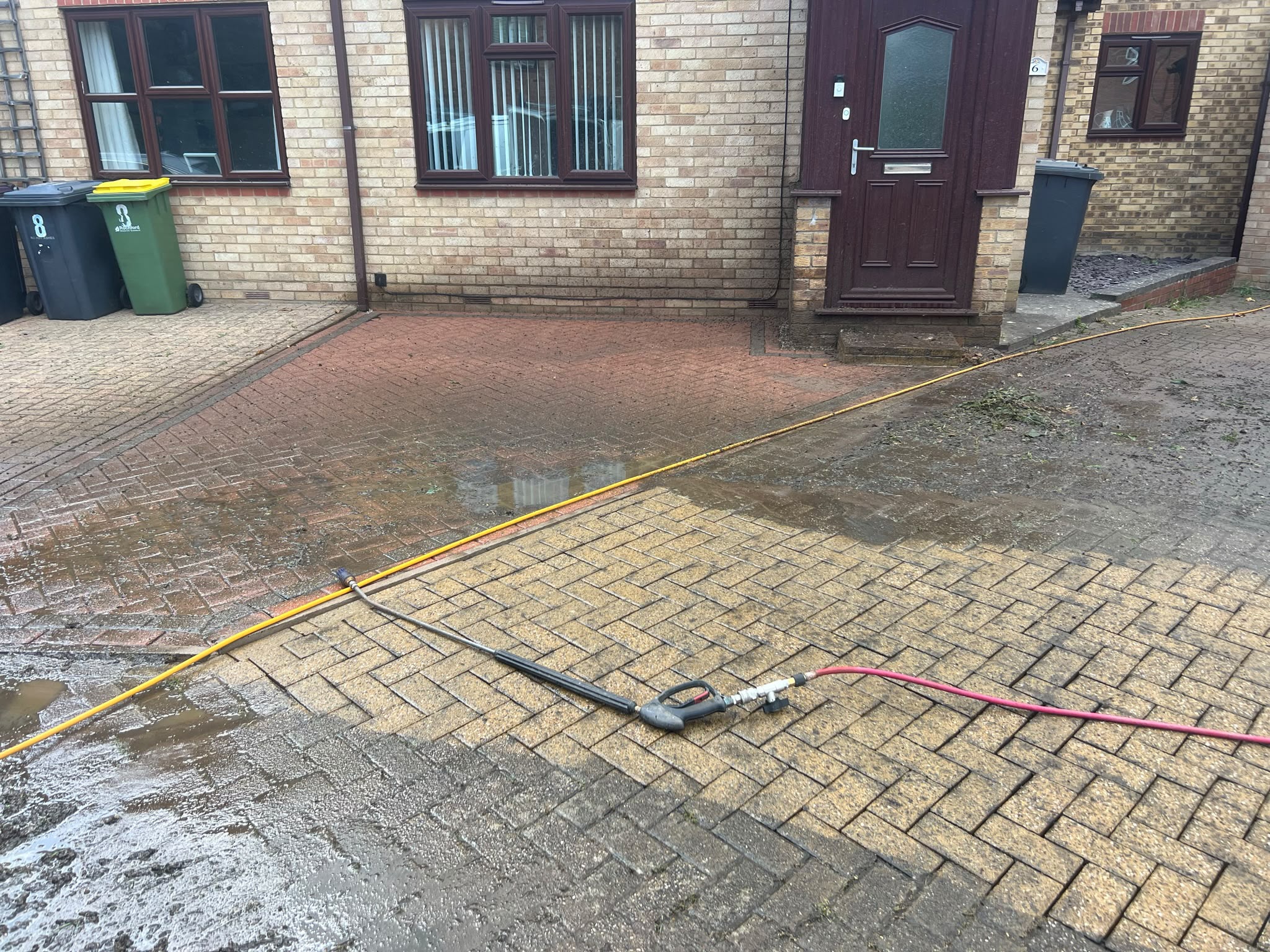 Block-paved driveway with a clean light section contrasting dark dirty paving, wand and hoses on the surface