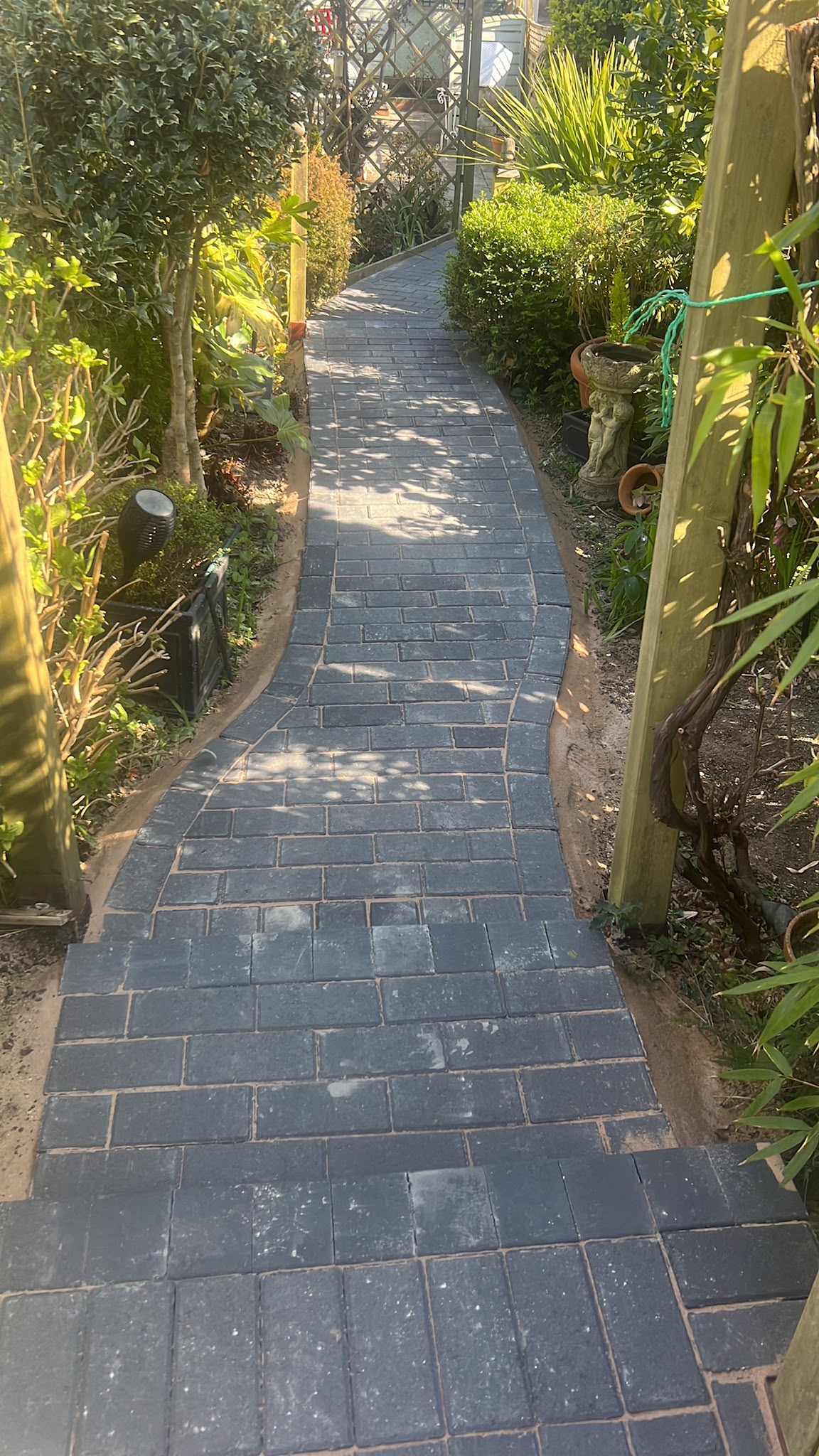 New dark grey block-paved steps leading into a curved garden path through lush planting