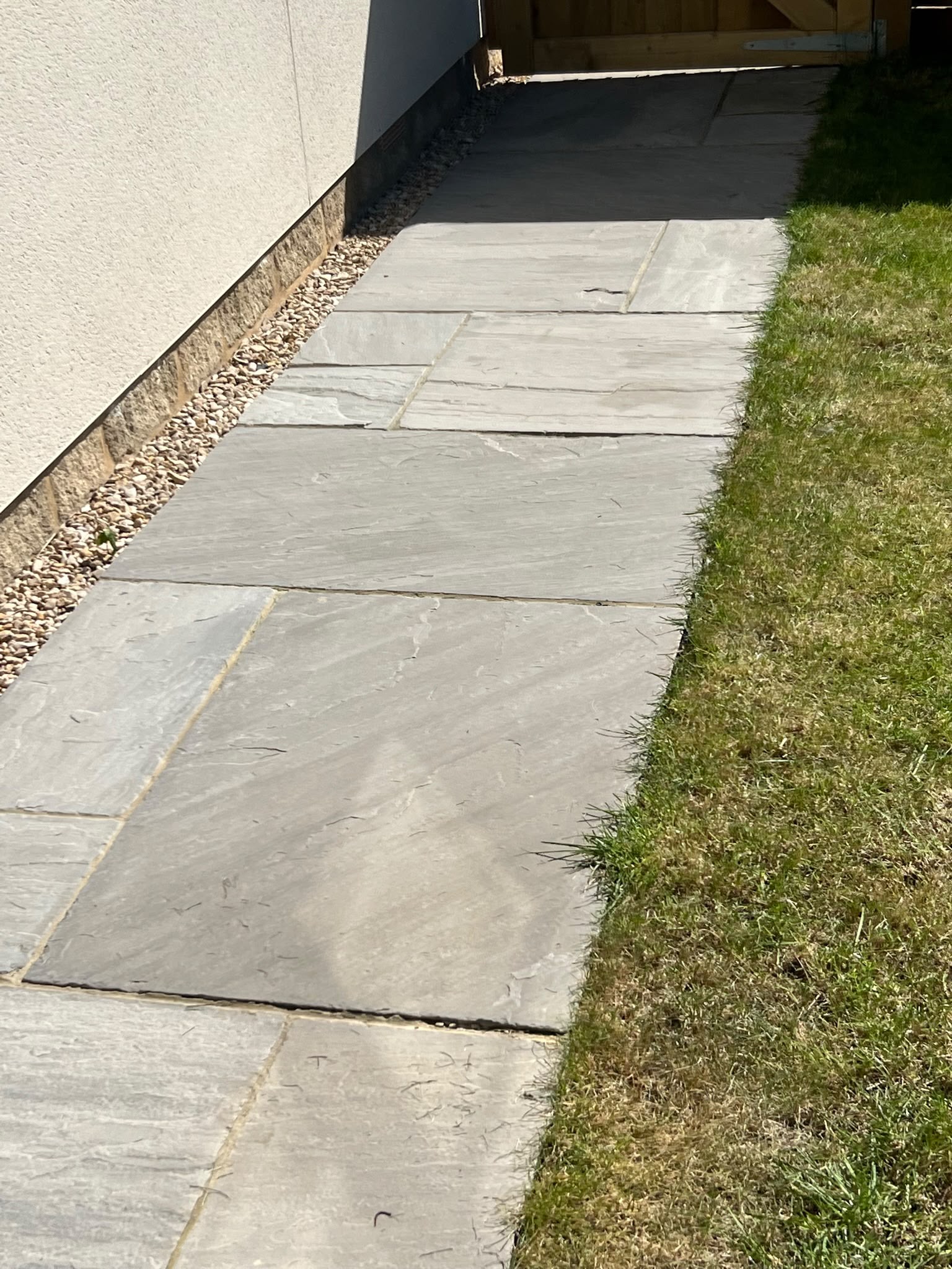 New grey natural stone paving path beside a white rendered wall and lawn leading to a wooden gate