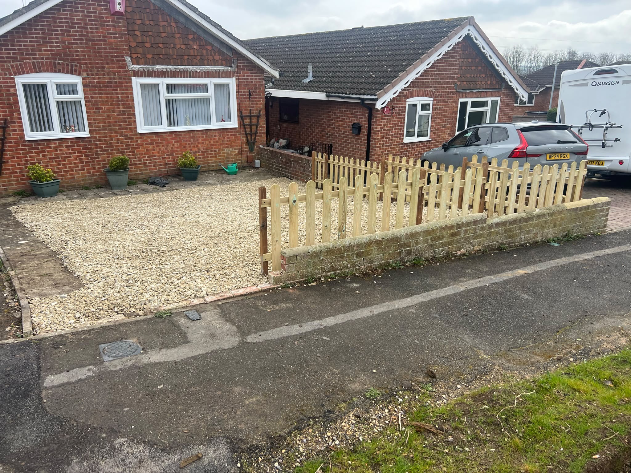 New light wooden picket fence on a low brick wall with fresh gravel in front of red brick bungalows
