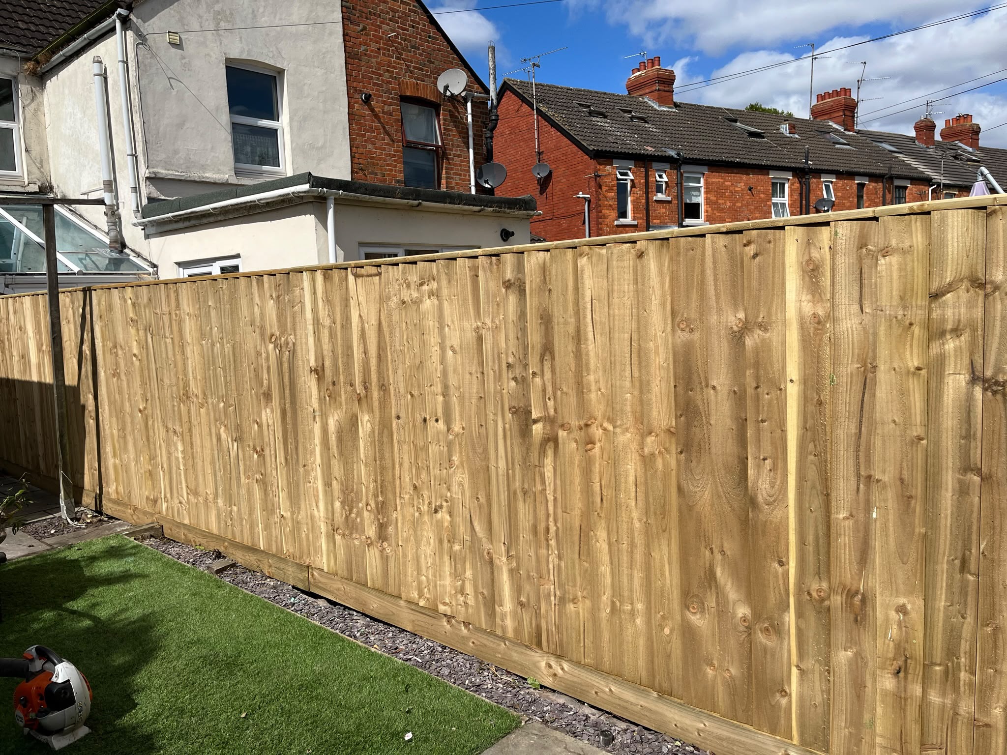 New light timber closeboard fence with capping rail beside artificial grass and slate chippings