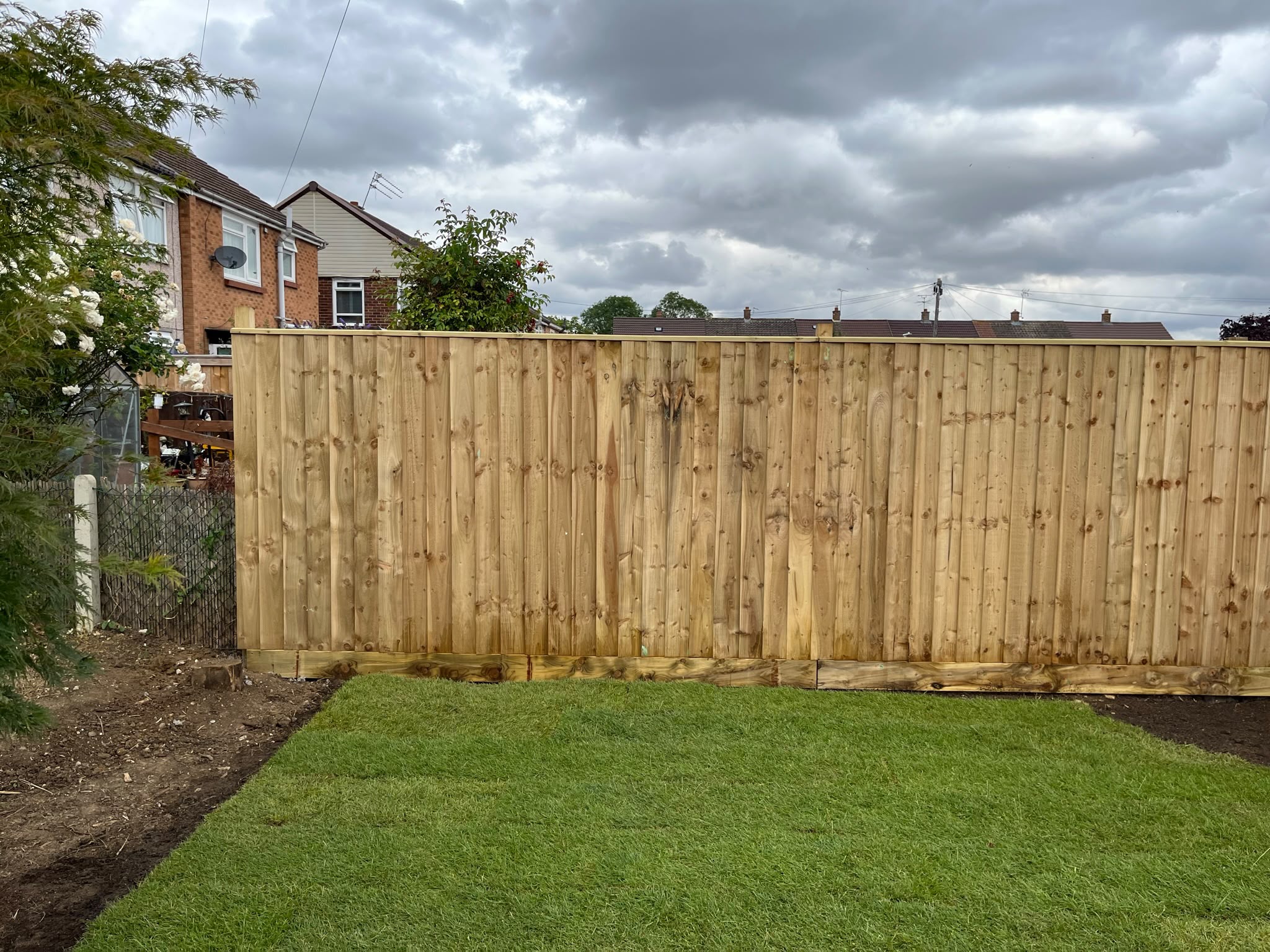Tall new featheredge fence with gravel boards in front of freshly laid turf and neighbouring rooftops