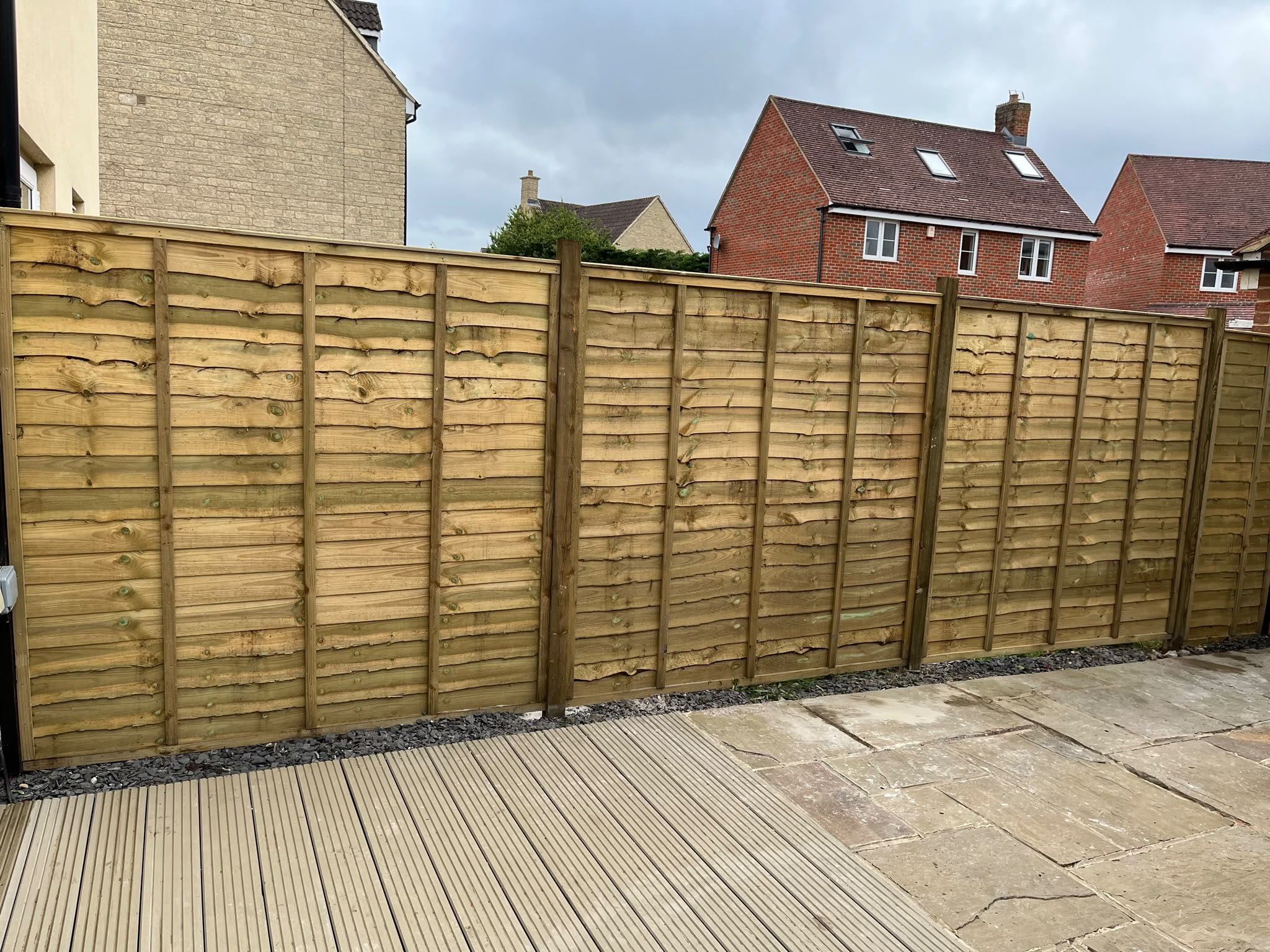 Fresh light brown wooden lap panel fence with gravel border beside decking and stone paving