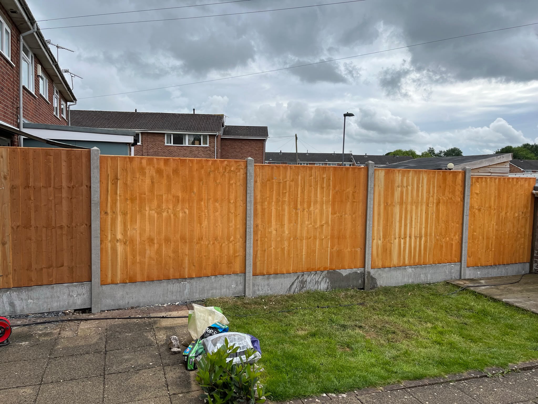 Line of orange-brown featheredge fence panels in concrete posts and gravel boards along a suburban garden