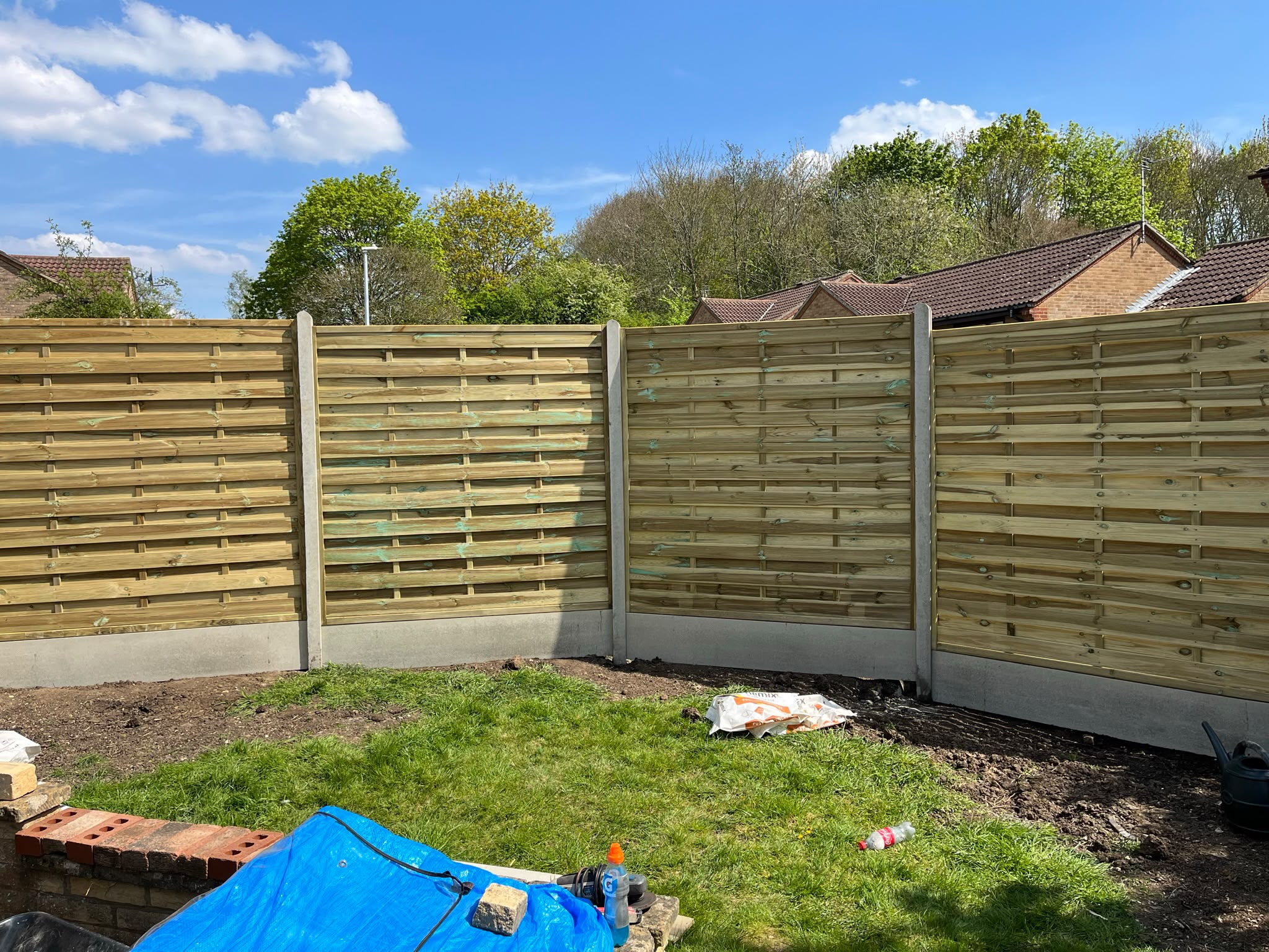 Four new horizontal wooden slat fence panels in concrete posts and gravel boards under a blue sky
