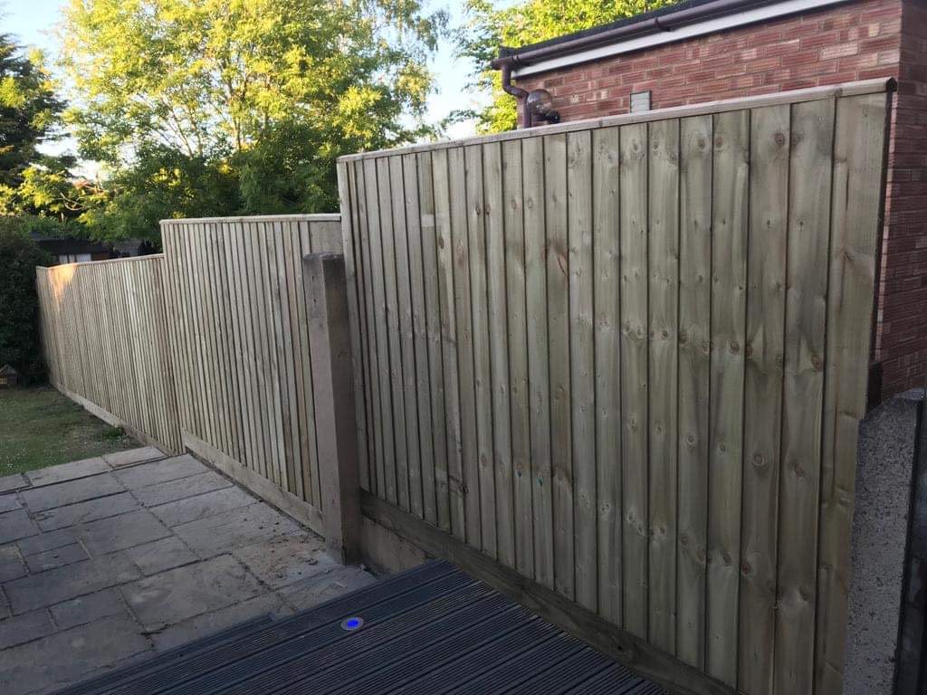 New light timber stepped closeboard fence beside stone paving and dark decking under blue sky
