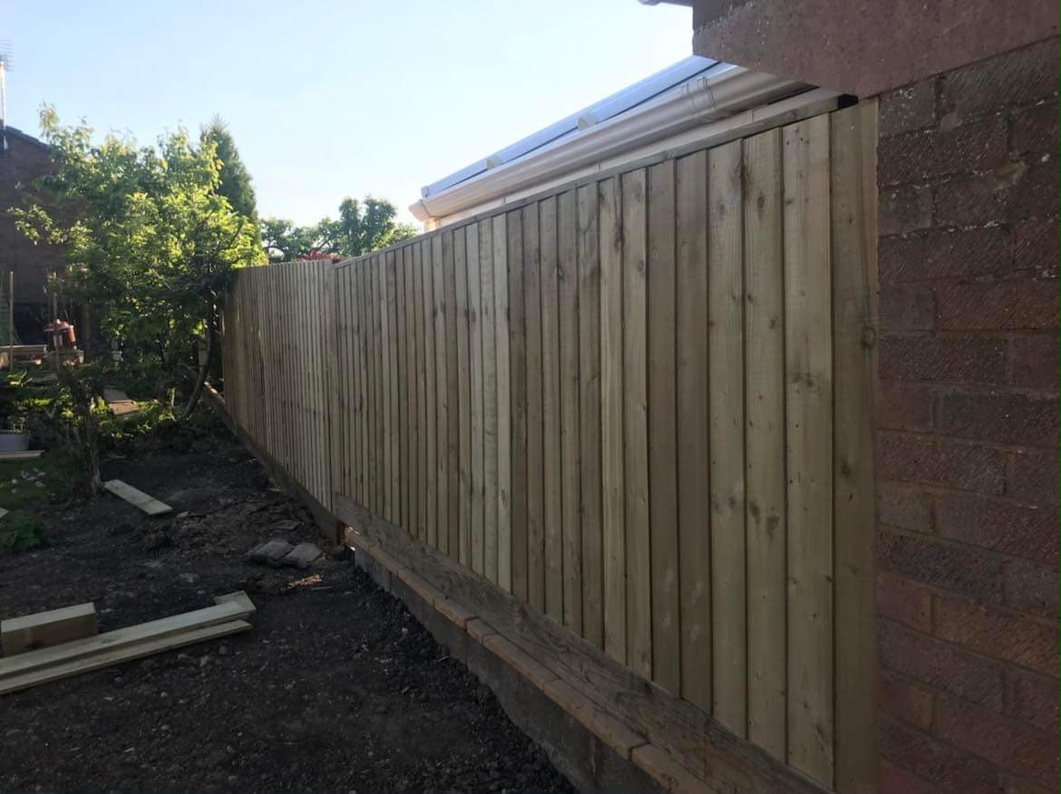 New closeboard wooden fence attached to a red brick wall with freshly turned soil along the base