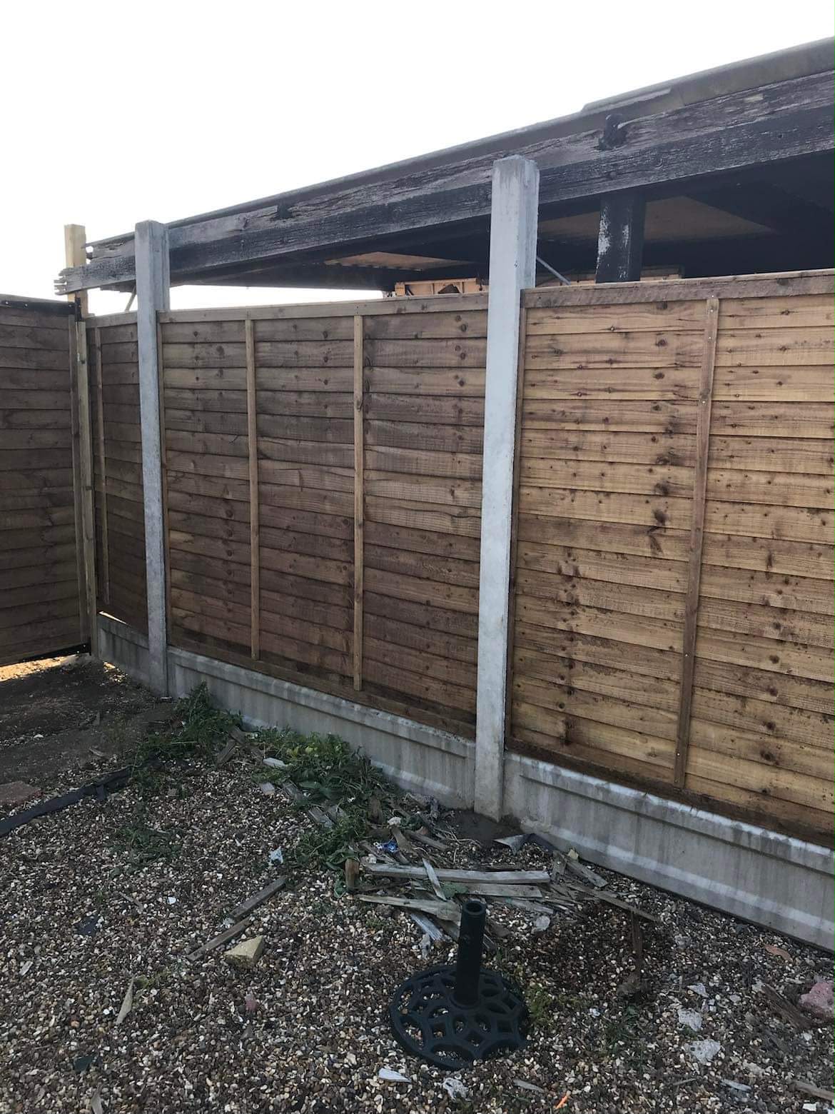 Brown-stained wooden lap fence panels in concrete posts and gravel boards on a gravel surface
