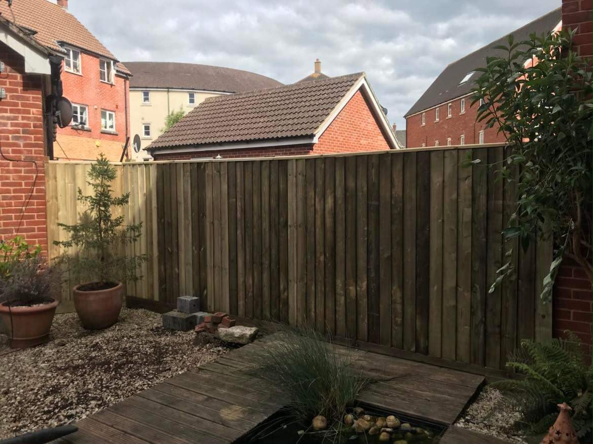 New vertical timber fence with capping rail behind a deck, small pond, gravel, and terracotta pots