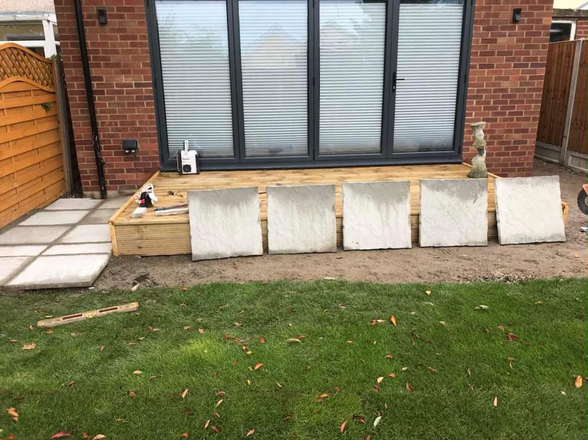 New timber deck under bifold doors with large paving slabs leaned ready and prepared ground in front