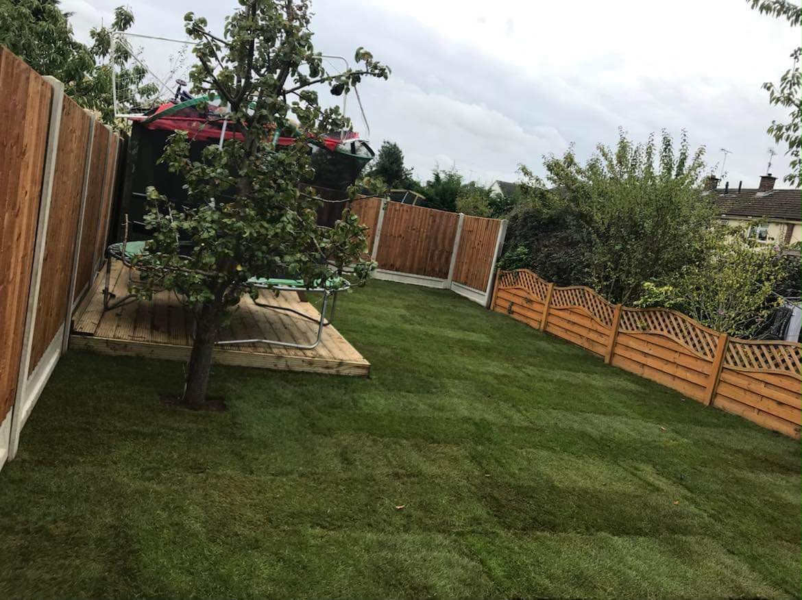 Freshly laid green turf lawn enclosed by timber fencing with a small deck and trampoline under overcast sky