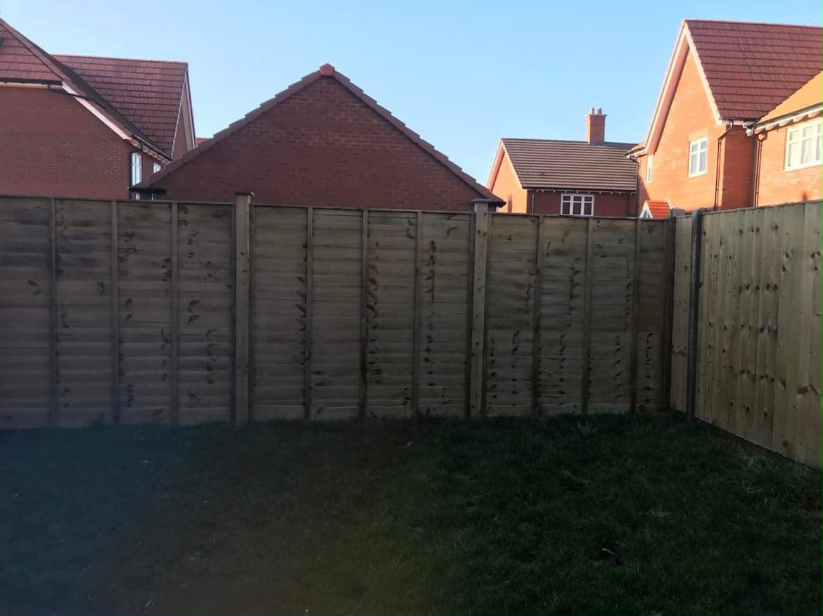 New wooden overlap panel fence forming a garden corner with lawn in front and brick houses behind
