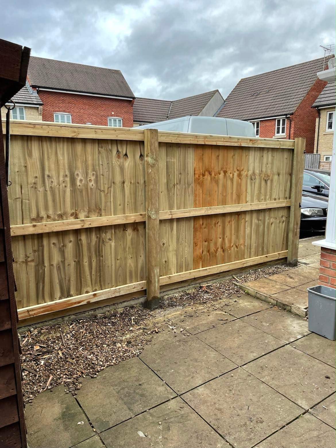 Newly installed wooden closeboard fence with timber posts beside a concrete slab patio and brick houses
